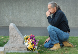 Man sitting at gravesite with a look of sadness